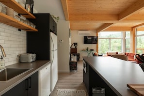 Une cuisine moderne avec un plafond en bois, un coin repas doté d’une grande table et un téléviseur fixé au mur.