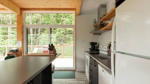 A modern kitchen with a large window, wooden ceiling, and a view of a deck.