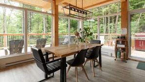A spacious room with a wooden table, chairs, and large windows offering a forest view.