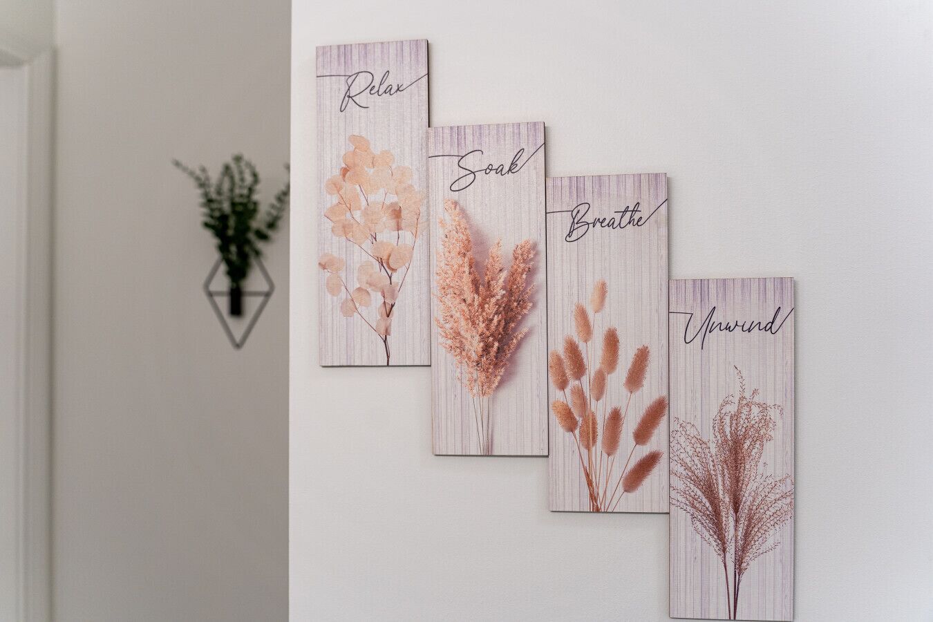 A wall with four framed artworks depicting plants and the words "Relax," "Soak," "Breathe," and "Unwind."