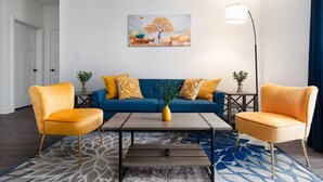 Un salón con un sofá azul, dos sillones amarillos, una mesita de centro y una lámpara de pie.