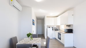 A modern kitchen with white cabinets, a dining area with a table and chairs, and a hallway leading to another room.