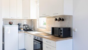 A modern kitchen with white cabinets, a built-in oven, a microwave, and a coffee machine.