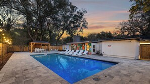 A swimming pool with lounge chairs, a covered seating area, and a building with a colorful mural. - Gator Grove (Gainesville)