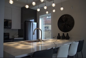 Una cocina moderna con encimera de mármol, electrodomésticos de acero inoxidable e iluminación colgante.