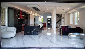 Una cocina moderna con una campana extractora roja, una zona de comedor con un sofá negro y una mesa, y una escalera que lleva a otro nivel.