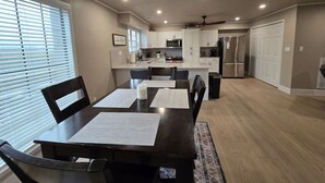 Une cuisine moderne avec des meubles blancs, des appareils en acier inoxydable et un coin repas comprenant une table et des chaises en bois foncé.