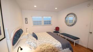 A bedroom with a bed, a bench, a chair, a window, and a mirror.