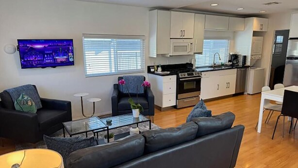 Uma sala de estar moderna com um sofá preto, uma mesa de centro e uma TV fixada na parede.