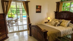 A bedroom with a bed, a nightstand, a lamp, a dresser, and a window with curtains. - Moradia com piscina privada em residência fechada, totalmente equipada (Sosúa)
