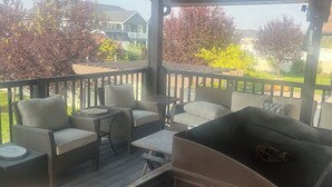 Un patio techado al aire libre con mobiliario de mimbre, una parrilla y vistas del barrio.