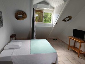 Um quarto pequeno e acolhedor, com uma cama, uma televisão sobre um suporte de madeira e uma janela que permite a entrada de luz natural.