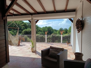 A covered patio with a wicker sofa, a hammock, and potted plants.