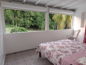 A bedroom with a bed, a chair, and a window with a view of greenery.
