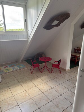 Una habitación con techo inclinado, una ventana, una mesa redonda con sillas, un tapete con estampados de animales y una pared verde.