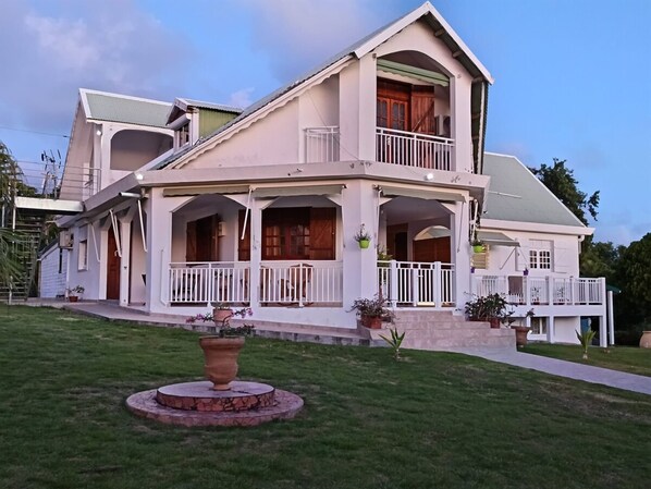 Uma casa de dois andares com varanda, alpendre e um jardim circular.
