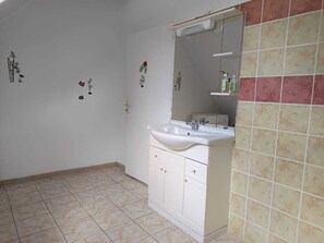Casa de banho com lavatório branco, espelho e chão em azulejos.