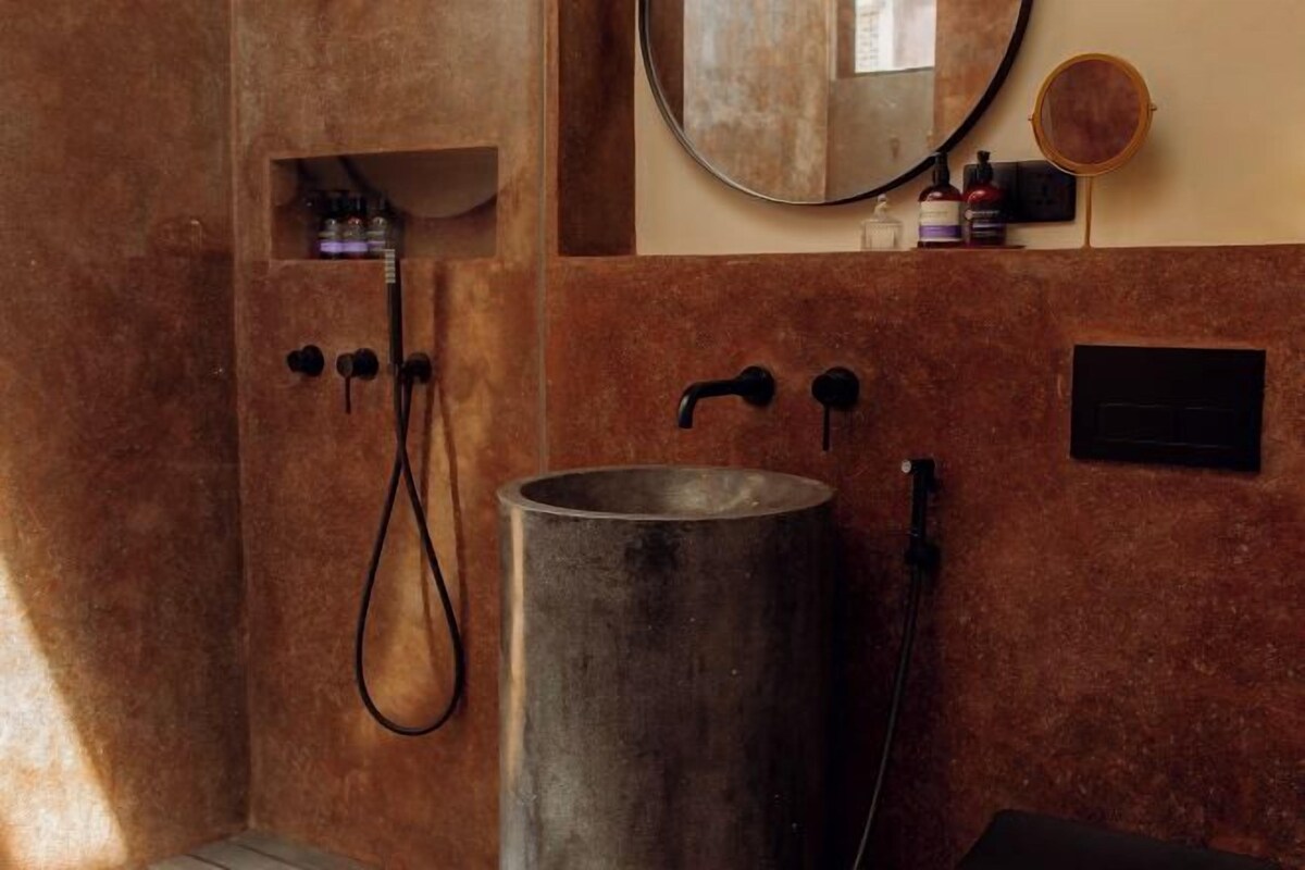 Une salle de bain avec un grand lavabo en métal, une douche dotée d’un panneau de commande et un miroir au mur.