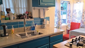 Une cuisine avec des meubles de rangement bleus, un évier, une cuisinière et une fenêtre avec des rideaux.