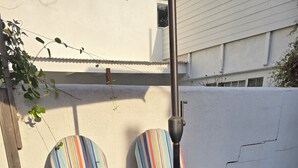 Deux fauteuils à rayures, une table ronde placée devant eux, un bac à fleurs en béton orné de feuilles et un mur blanc avec une fenêtre.