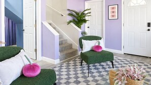 Ein Zimmer mit Schachbrettfußboden, grünen Polsterstühlen, einer Treppe und einer Tür mit weißem Rahmen.