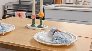 Eine Küche mit einem Holztisch, zwei weißen Tellern, einem blauen Tuch und zwei Kerzen.