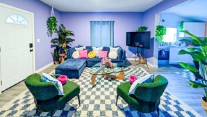 Ein Wohnzimmer mit einer Couch, zwei Sesseln, einem Couchtisch, einem Fernseher und einer Küche im Hintergrund.