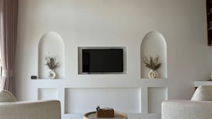 Una sala de estar moderna con un televisor de pantalla plana montado en la pared, dos mesitas de noche con plantas decorativas y una mesa de centro redonda de madera.