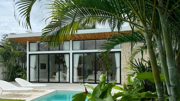 Una casa moderna con piscina, ventanas amplias y abundante vegetación.