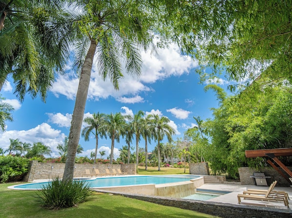 A pool area with lounge chairs, palm trees, and a stone wall.
