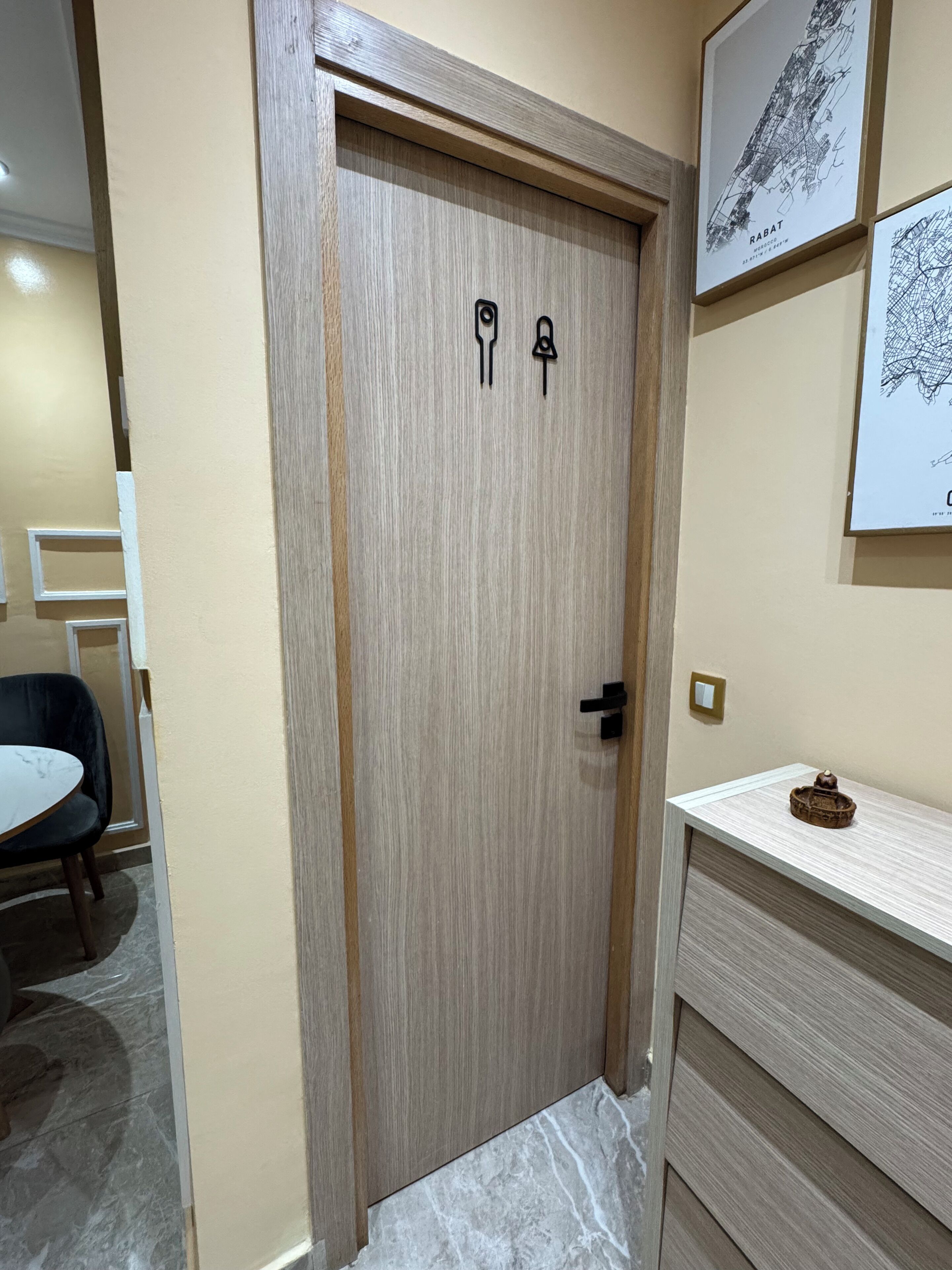 Uma porta de madeira com maçaneta e fechadura, uma mesa pequena com uma cadeira e um quadro pendurado na parede.
