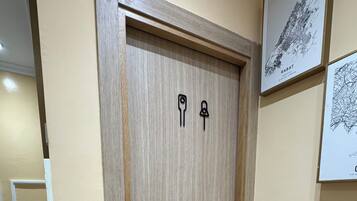Uma porta de madeira com maçaneta e fechadura, uma mesa pequena com uma cadeira e um quadro pendurado na parede.