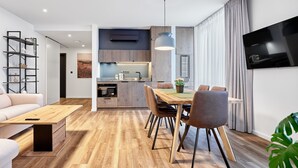 Een moderne woonkamer met een houten eettafel, banken en een aan de muur bevestigde televisie.
