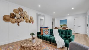 Ein modernes Wohnzimmer mit einem grünen Sofa, einem runden Holztisch mit Pflanze und einem farbenfrohen Teppich.