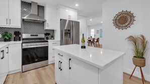 Une cuisine moderne avec des meubles blancs, des appareils en acier inoxydable et un îlot central.