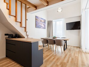 A modern kitchen with a wooden island, a dining area with a table and chairs, and a TV mounted on the wall.