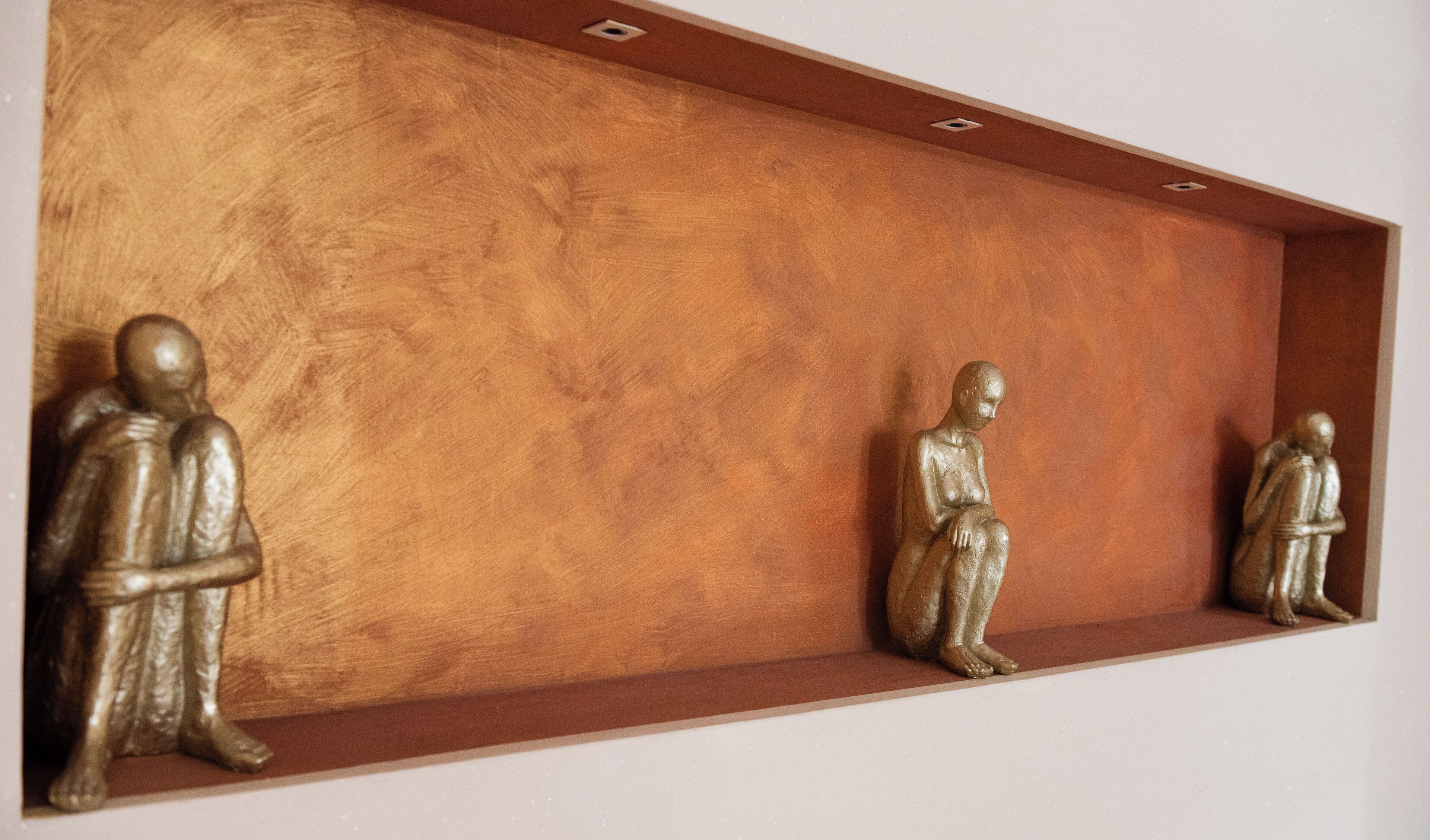 A wooden shelf with three bronze statues of seated figures.