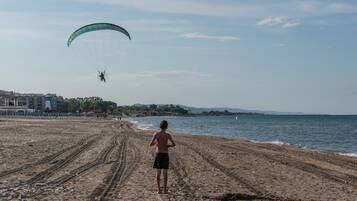 Una spiaggia con una persona in piedi che guarda un parapendio in lontananza.