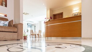 A hotel reception area with a wooden reception desk, a sofa, and a patterned floor.