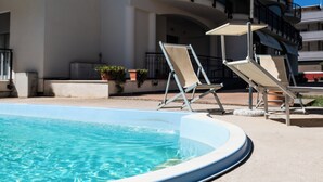 A pool area with lounge chairs and an umbrella, surrounded by a multi-story building with balconies.