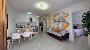 Eine moderne Küche mit weißen Schränken, ein Essbereich mit Tisch und Stühlen, eine Couch und ein Bett im angrenzenden Zimmer.