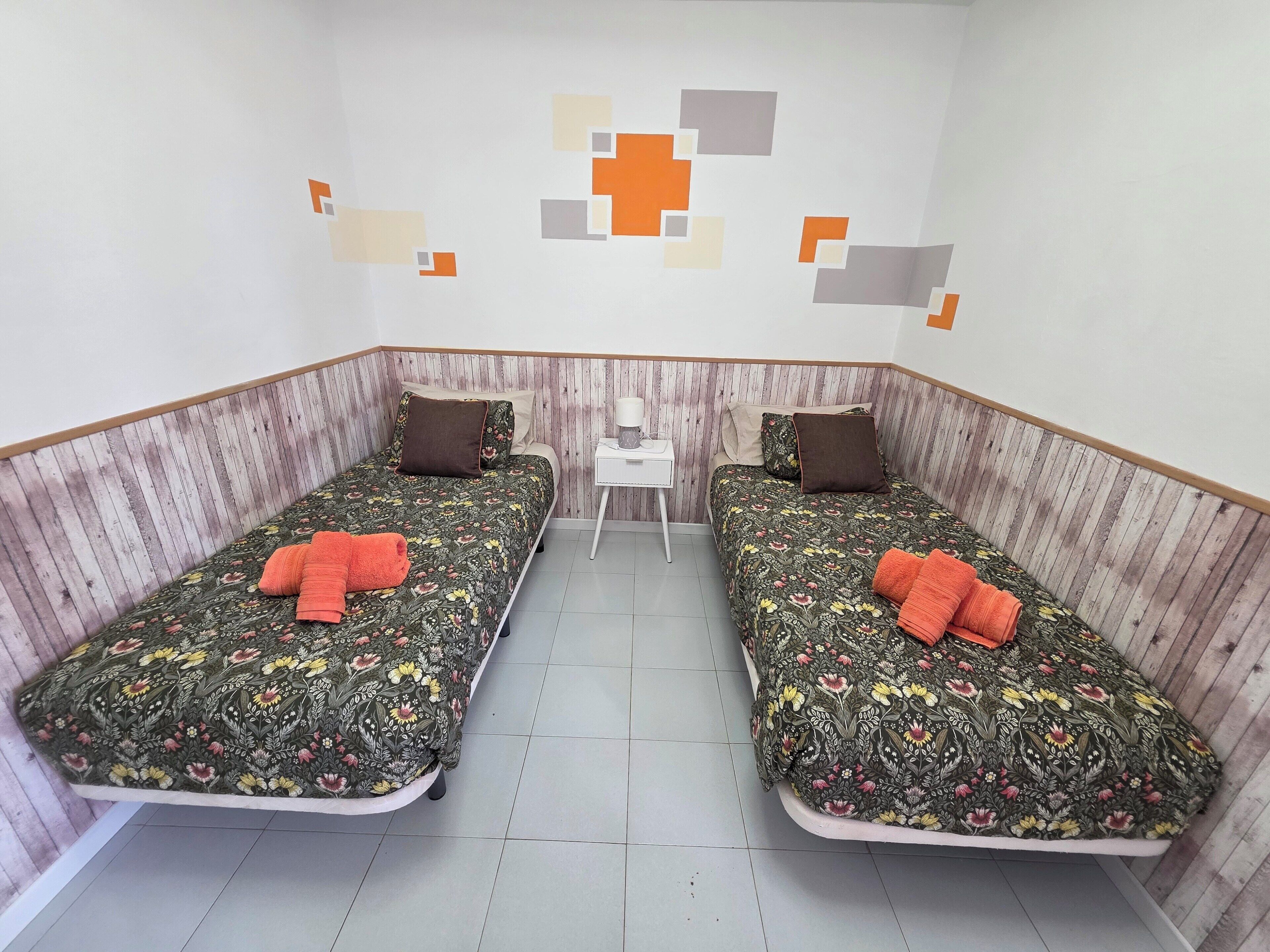 Una habitación con dos camas, una mesita y una pared con diseños geométricos.