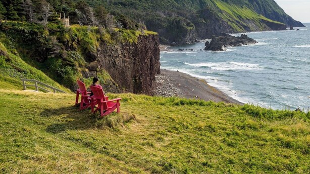 Eine Küstenlandschaft mit einer Klippe, dem Ozean und einer Person, die auf einem roten Stuhl sitzt.