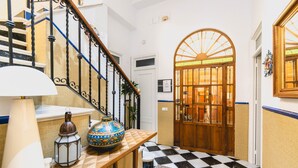 Una escalera con piso estampado, una puerta de madera con paneles de vidrio y un farol decorativo sobre una mesa.