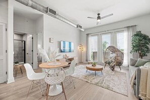 A spacious living room with a dining area, a ceiling fan, and a large window with blinds. - Dallas Dream Stay  Prime Location  1BR  2BEDS (Dallas)