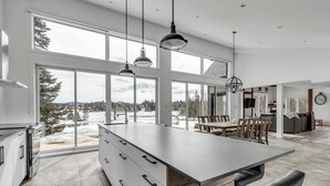 Ett modernt kök med en stor köksö, stora fönster och utsikt över ett snötäckt landskap.