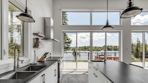 Ett modernt kök med en stor köksö, en inbyggd spis och utsikt över en sjö genom stora fönster.