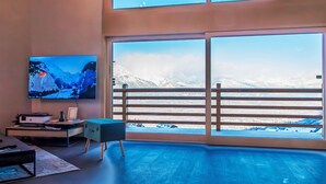 A modern living room with a large TV, wooden flooring, and a balcony with a mountain view. - Bike & Ski 301 by Interhome (Nendaz)