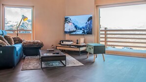 A modern living room with a large TV, comfortable seating, and a view of a snowy mountain landscape. - Bike & Ski 301 by Interhome (Nendaz)