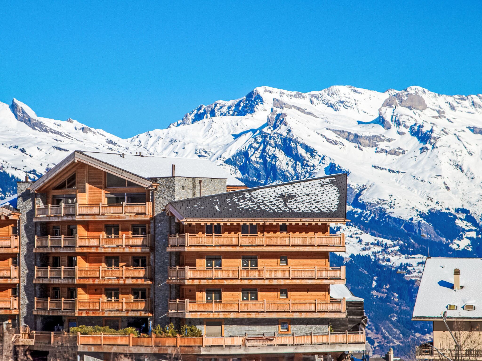 Un edificio de madera de varios pisos con balcones, con montañas nevadas al fondo.